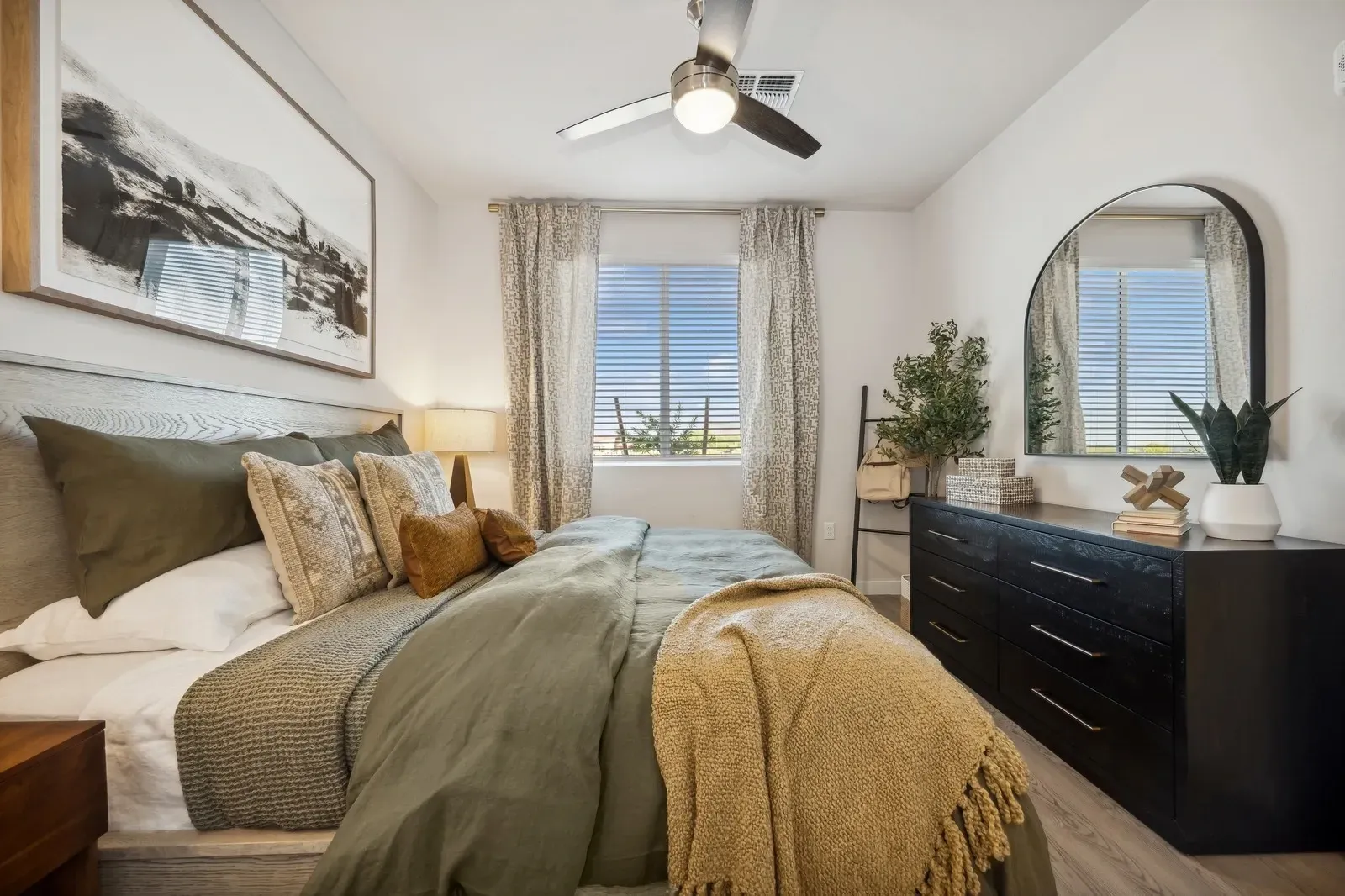 Cozy bedroom with a bed, dresser, windows with blinds, and neutral-toned decor