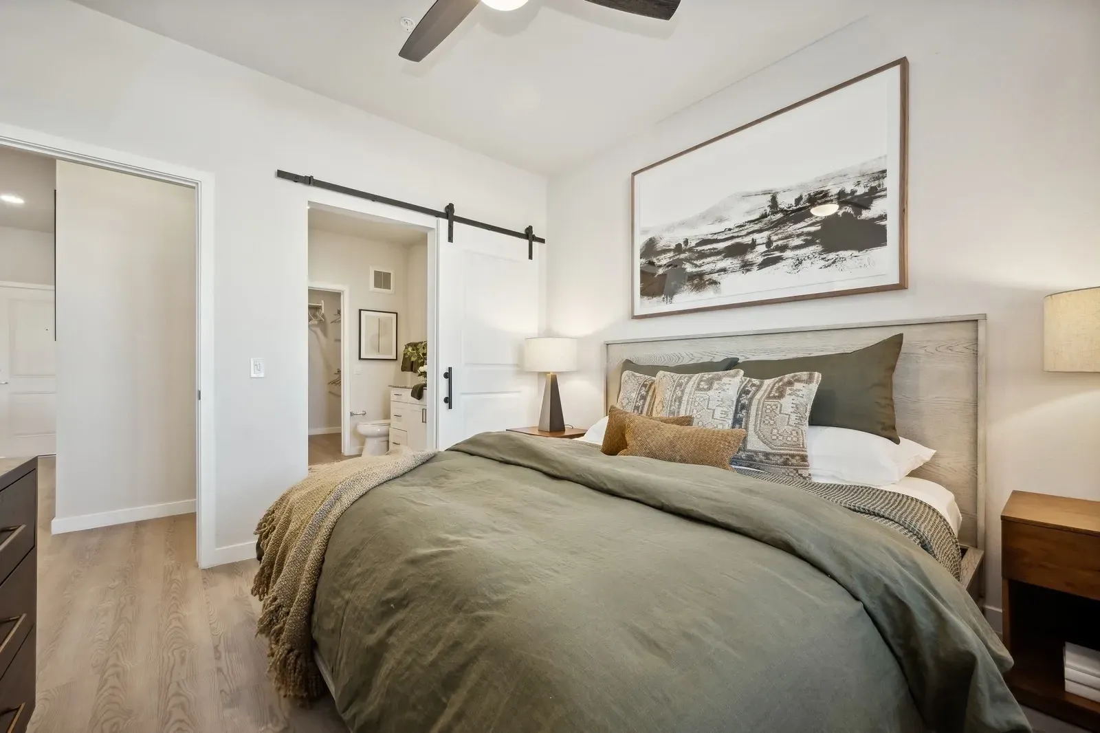 Cozy bedroom with a made bed, white walls, sliding barn door, and framed landscape art