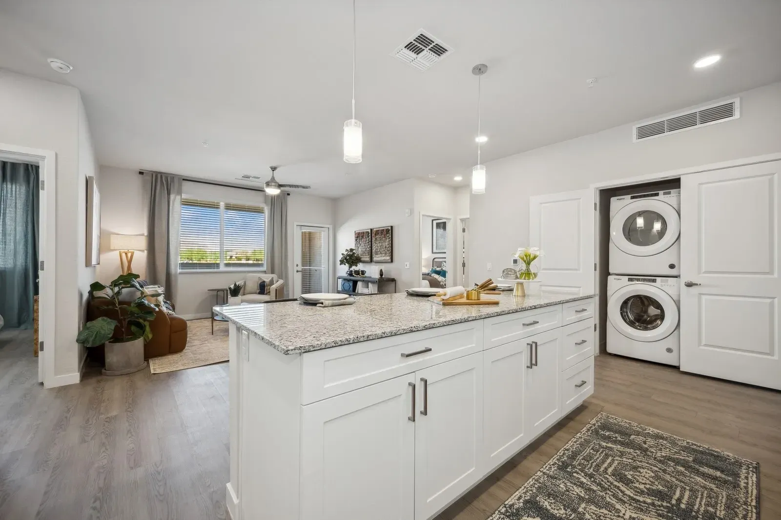 Bright modern kitchen with white cabinets, large island, pendant lights, and stacked washer-dryer.