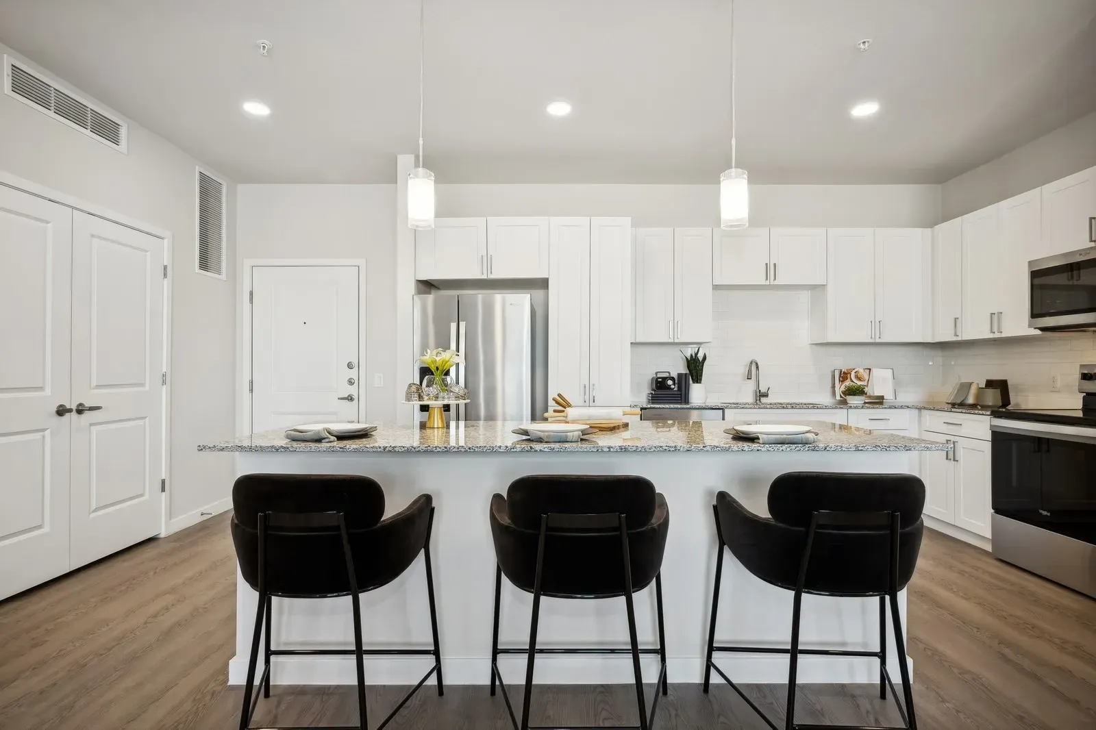 Stylish kitchen featuring a granite-topped island with three bar stools, white cabinetry, and stainless steel appliances.
