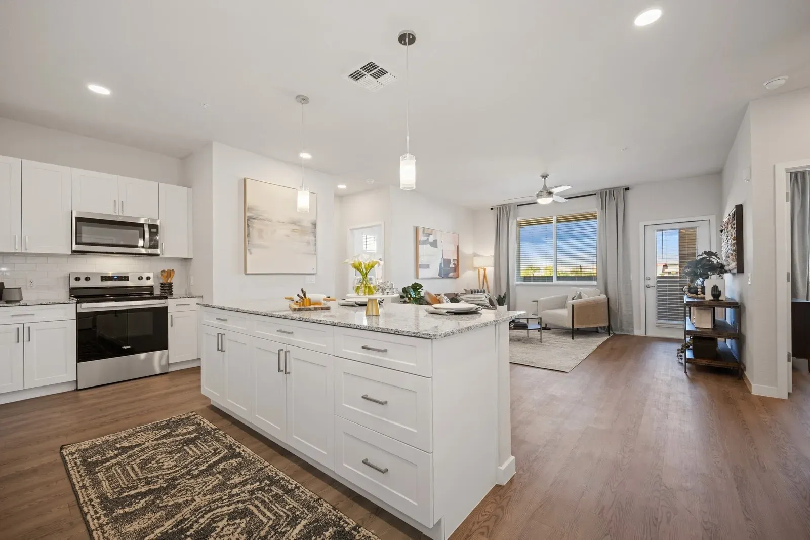 Modern white kitchen with island, three black stools, pendant lights, and stainless steel appliances