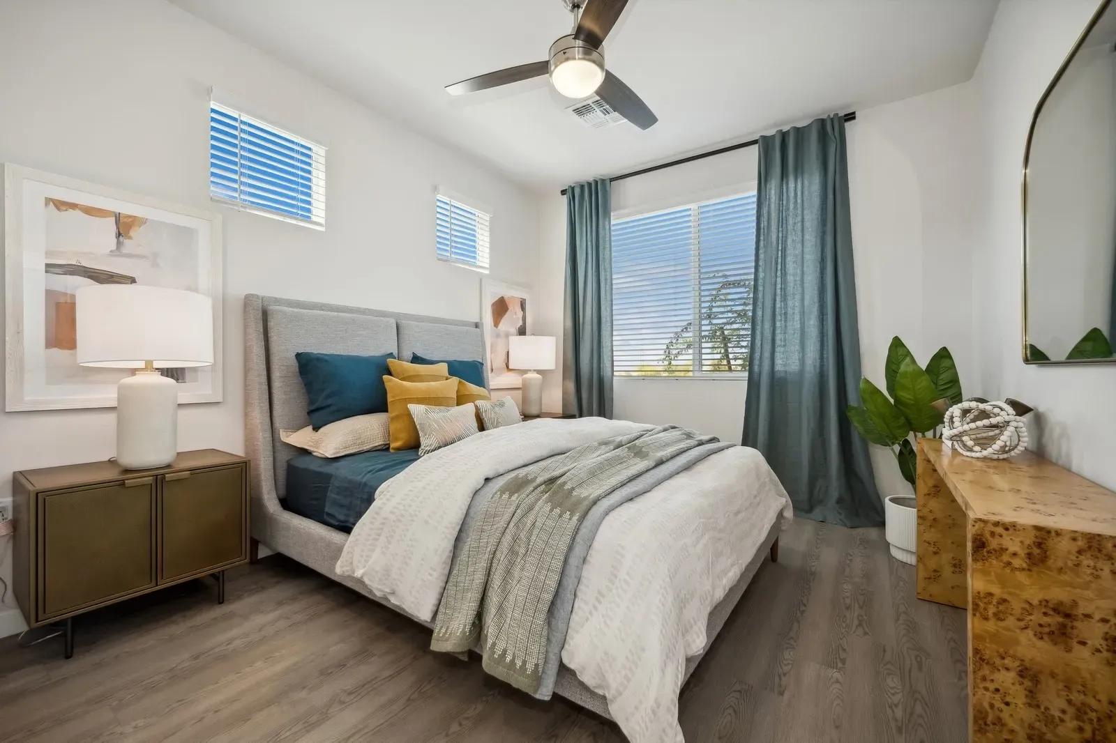 Bright modern bedroom with blue accents, a gray bed, ceiling fan, and window view of mountains