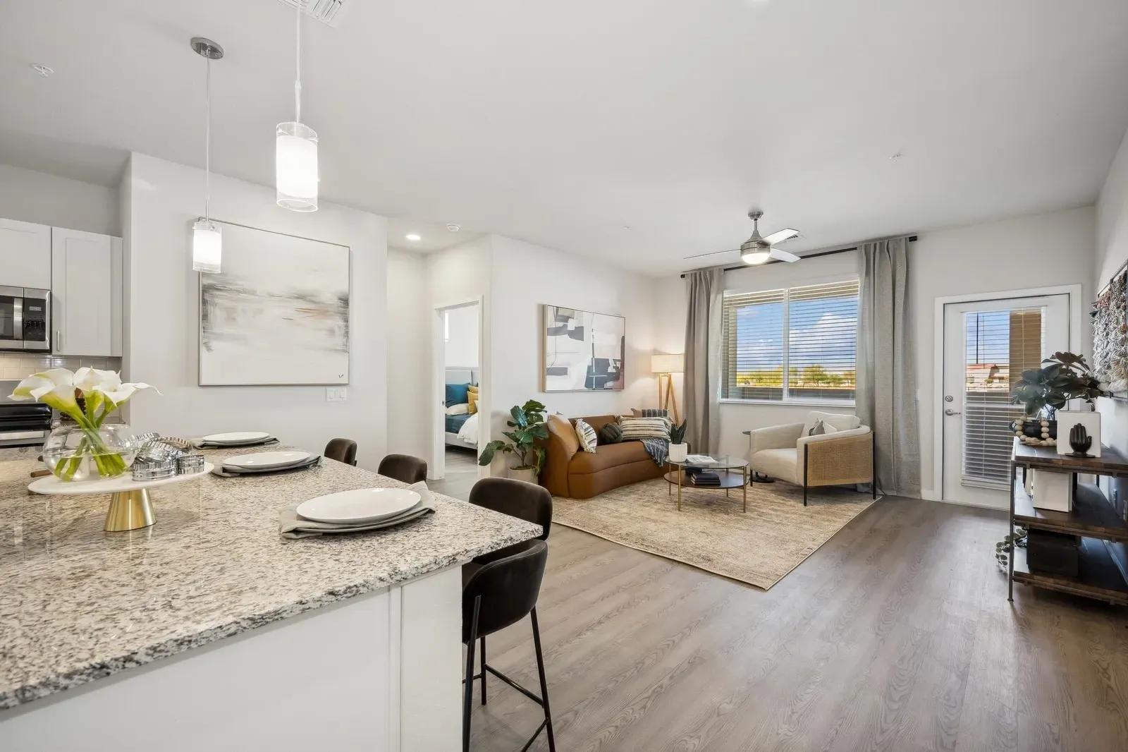 Bright open-plan living room with kitchen island, gray floors, beige sofa, and large windows.