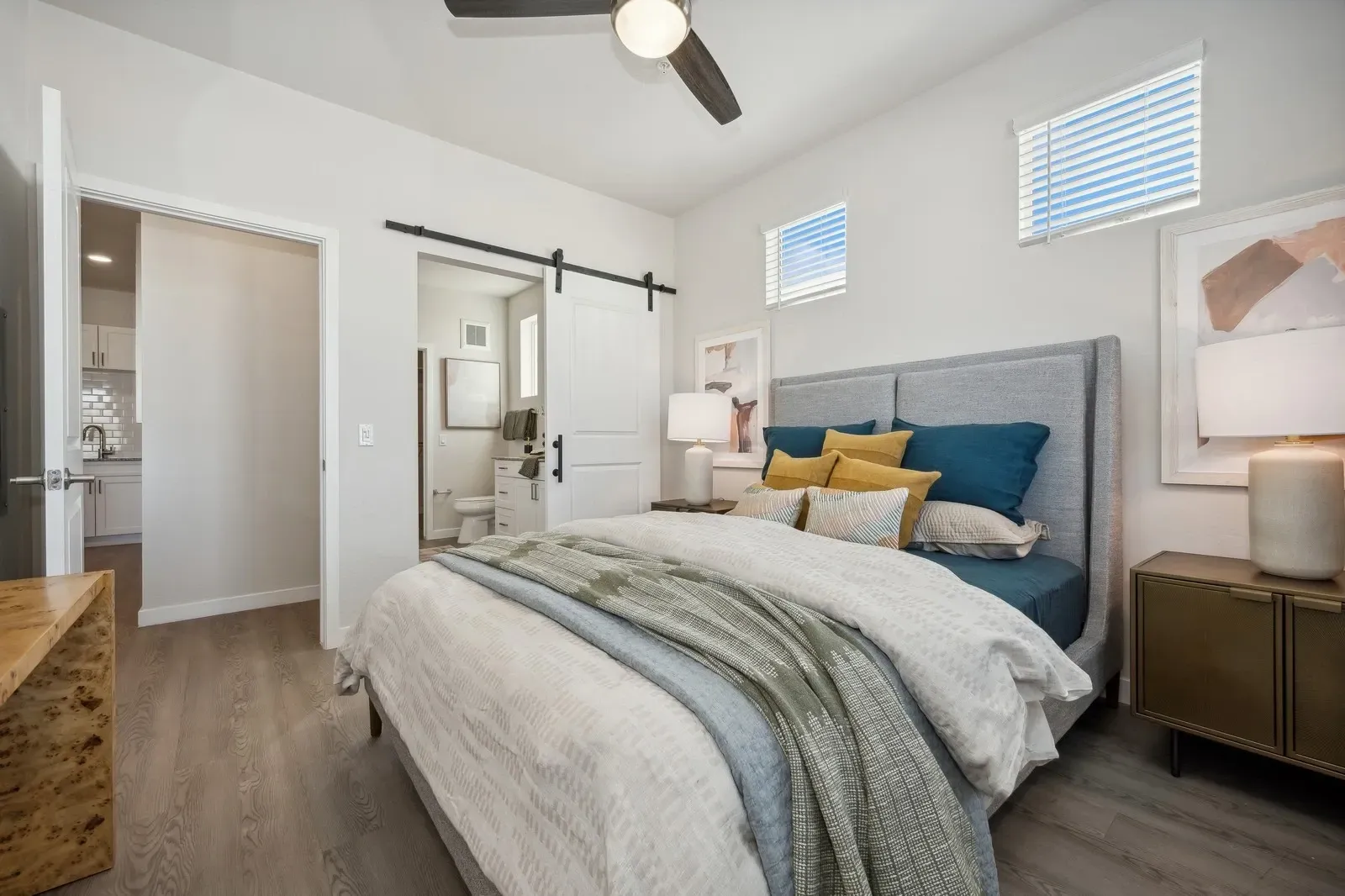 Bright bedroom with a bed, blue headboard, sliding barn door, and natural light from small windows