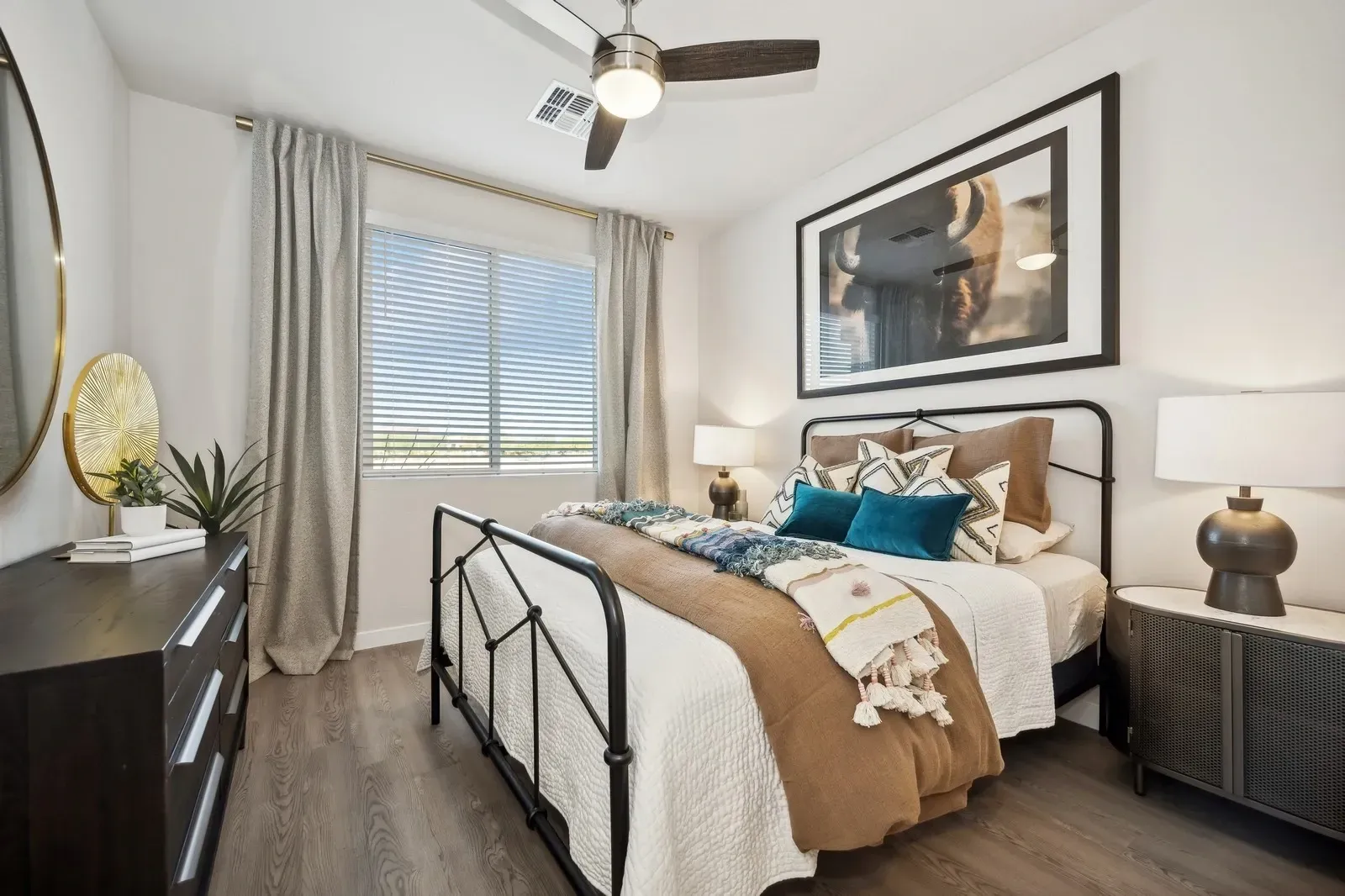 Bright bedroom with a black metal bed, neutral decor, bedside lamps, and a large window with curtains.