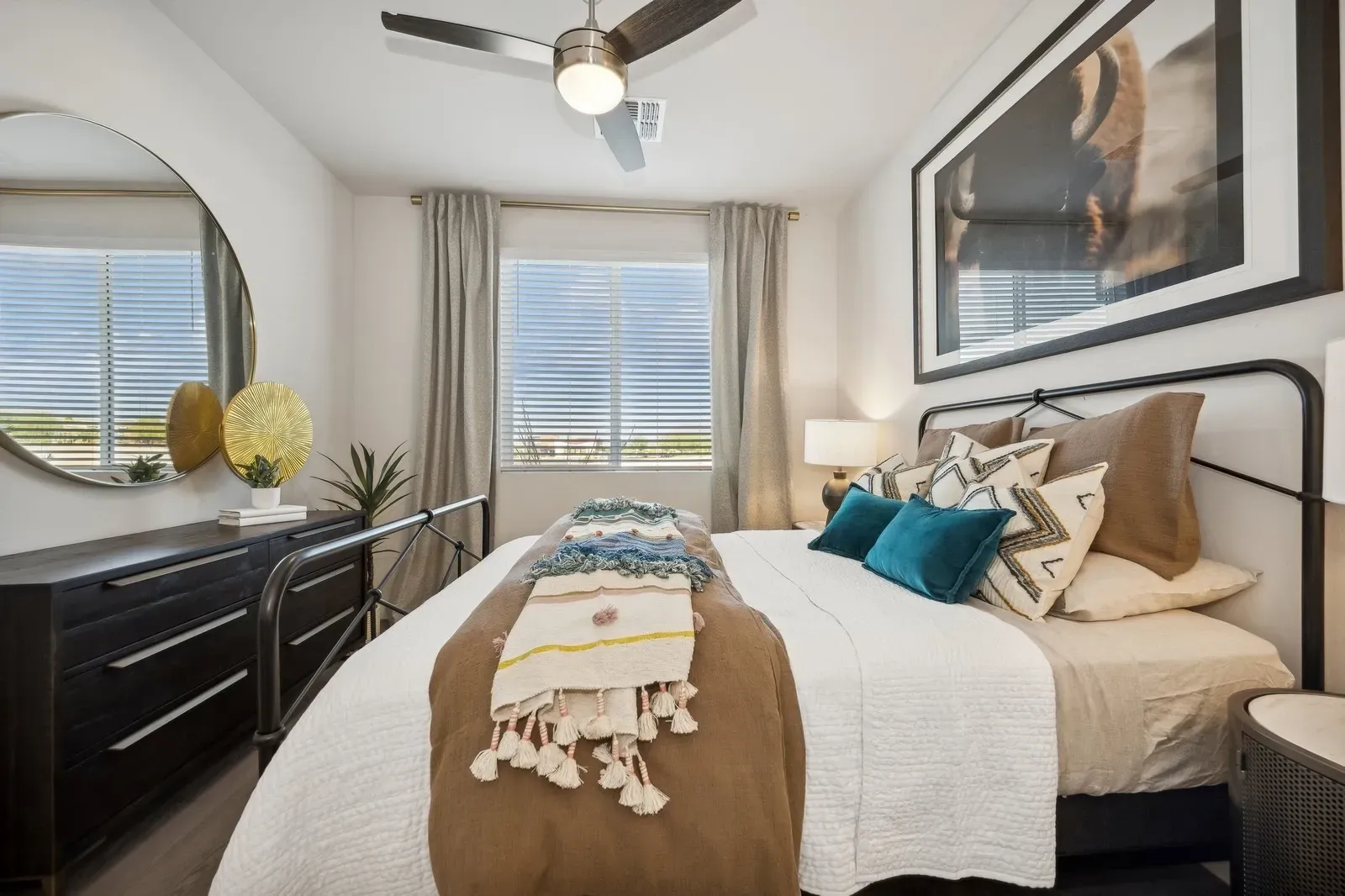 Bright bedroom with a bed, dresser, ceiling fan, and window with a city view.