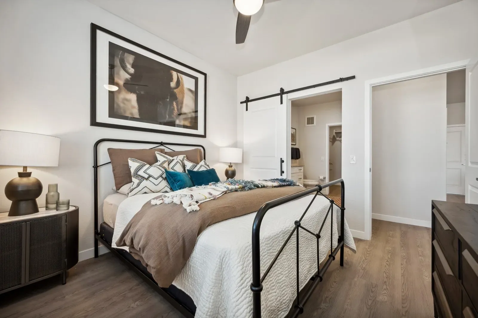 Bright modern bedroom with a black metal bed, white walls, wood floors, and framed wall art