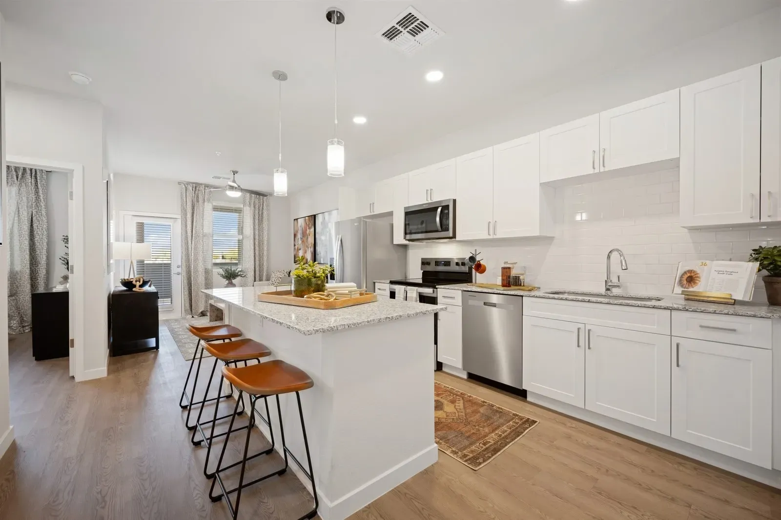 Bright white modern kitchen with island, bar stools, stainless appliances, and wood floors