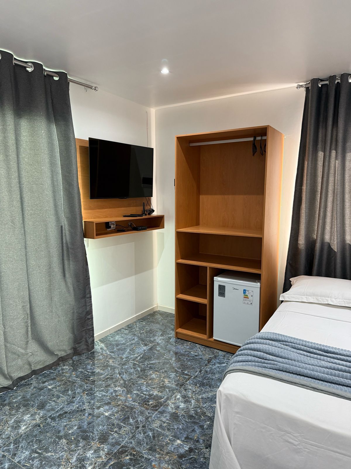 Um quarto de hotel com uma cama, uma televisão e uma geladeira.