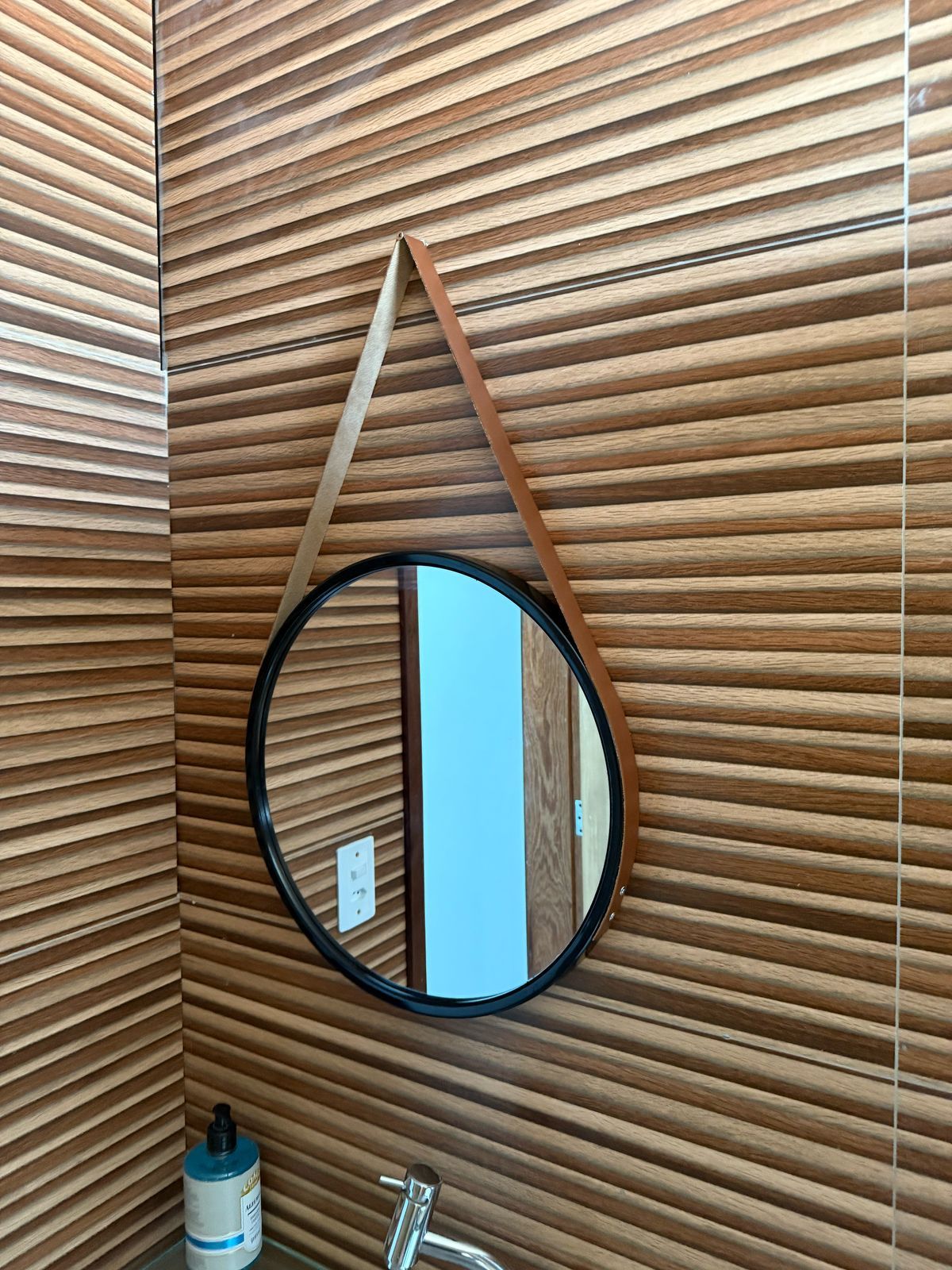 Um espelho redondo está pendurado em uma parede de madeira em um banheiro.