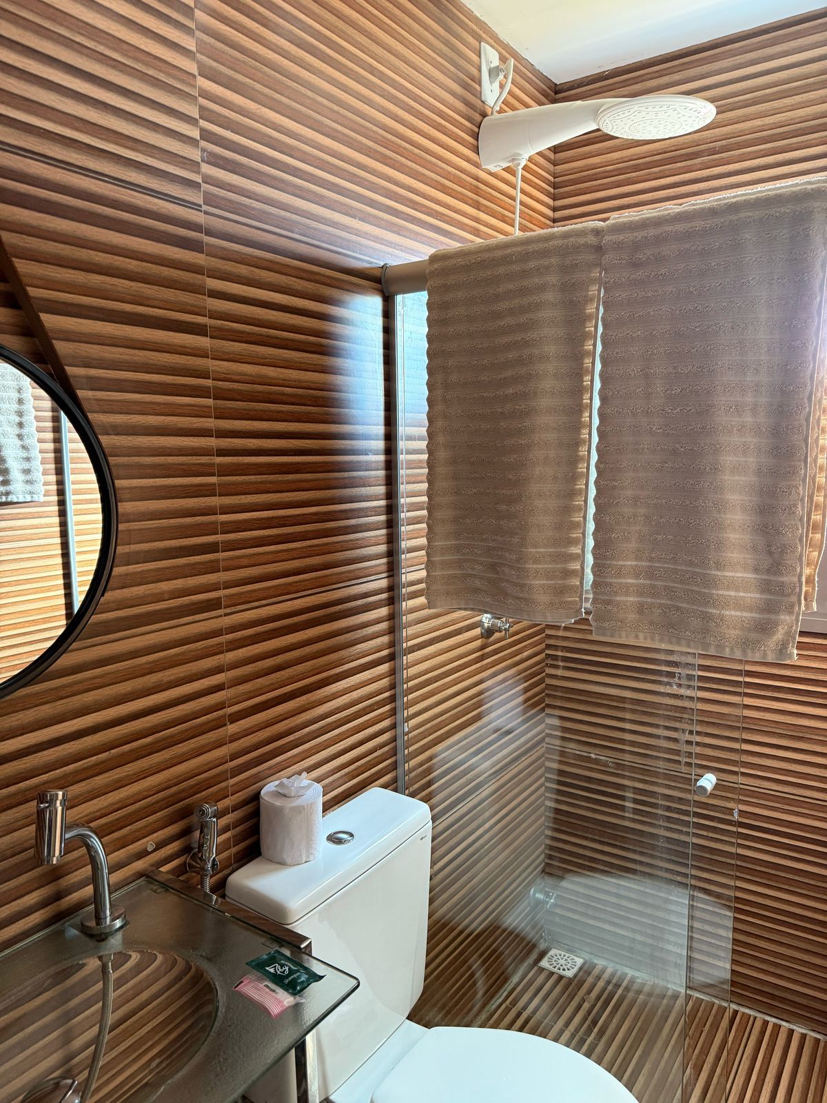 Um banheiro com vaso sanitário, pia, chuveiro e espelho.