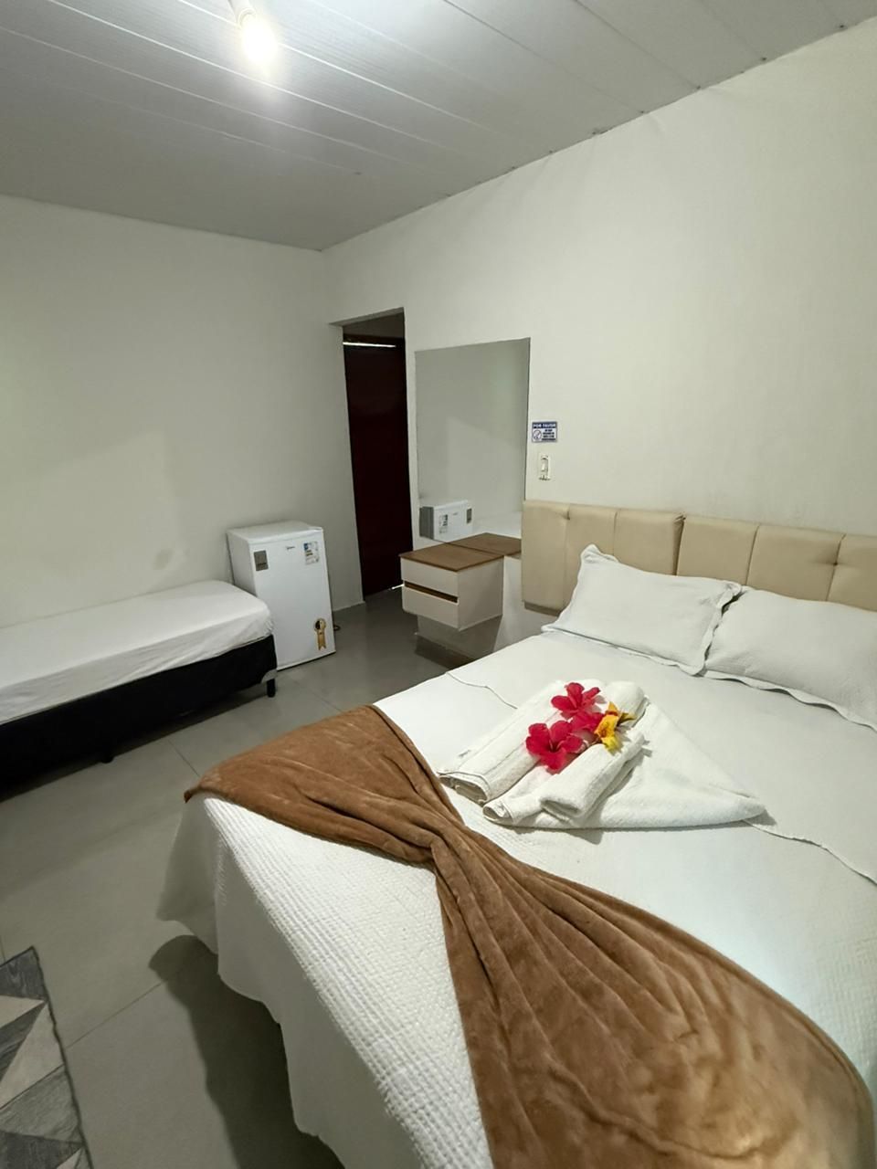 Um quarto com uma cama, duas camas, uma geladeira e um espelho.