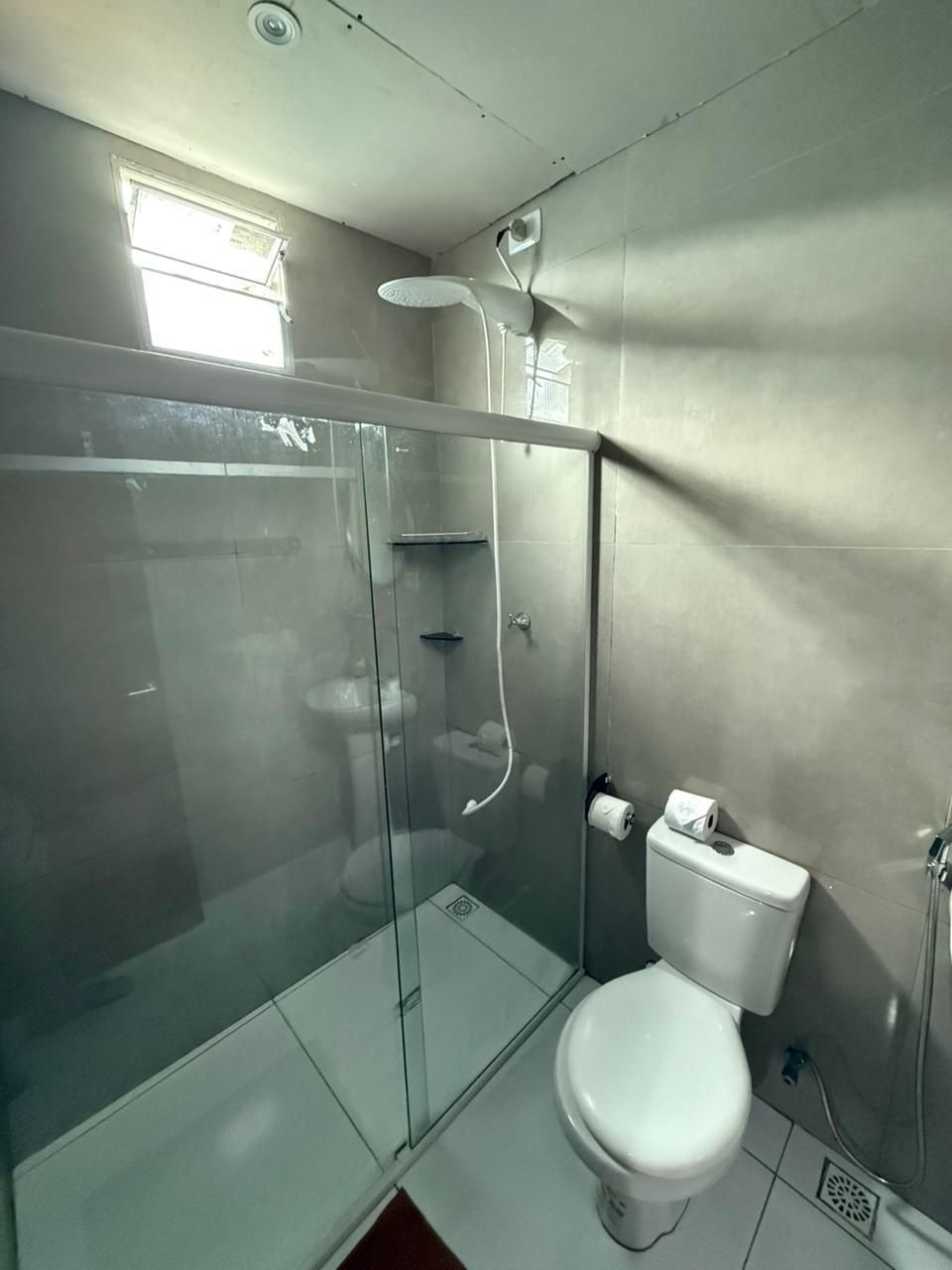 Um banheiro com vaso sanitário, chuveiro, pia e espelho.