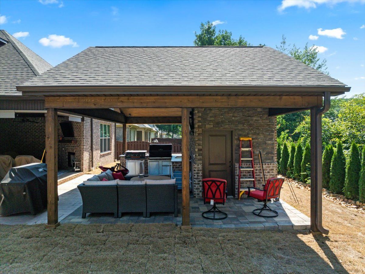 A large covered patio area with a couch , chairs , and a grill.