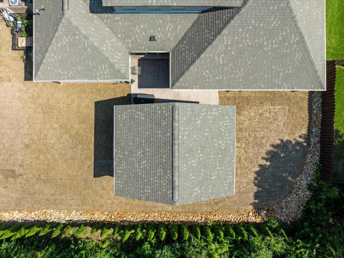 An aerial view of a house with a gray roof surrounded by trees.