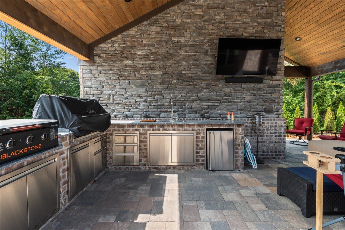 A large outdoor kitchen with a grill and a television.