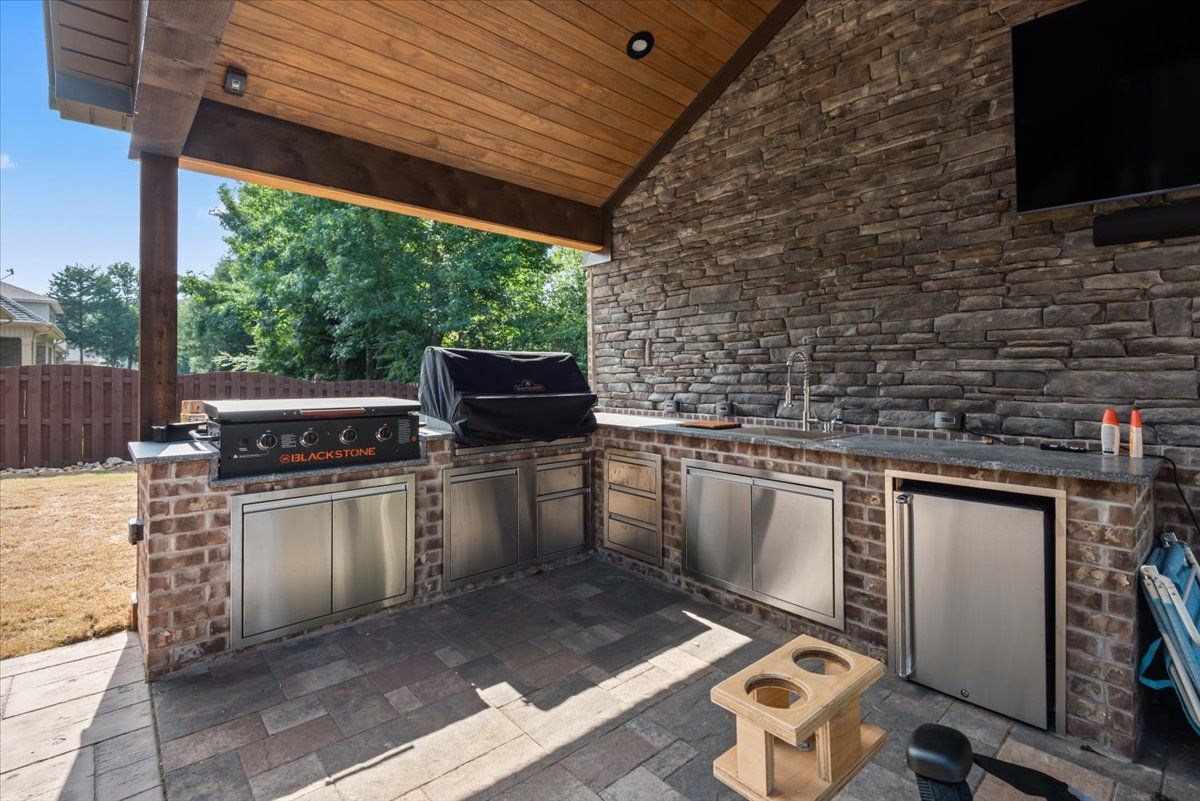 An outdoor kitchen with a grill , sink , refrigerator and television.