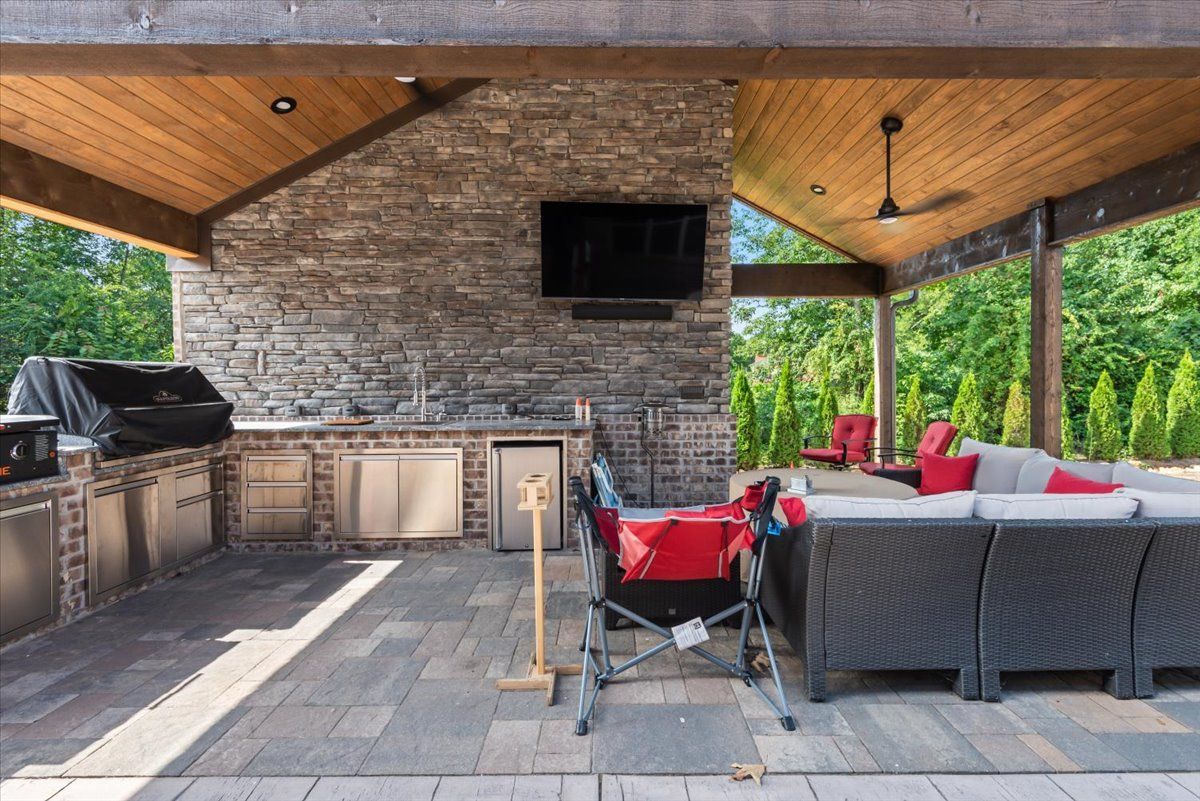 A patio with a grill , couch , chairs and a television.