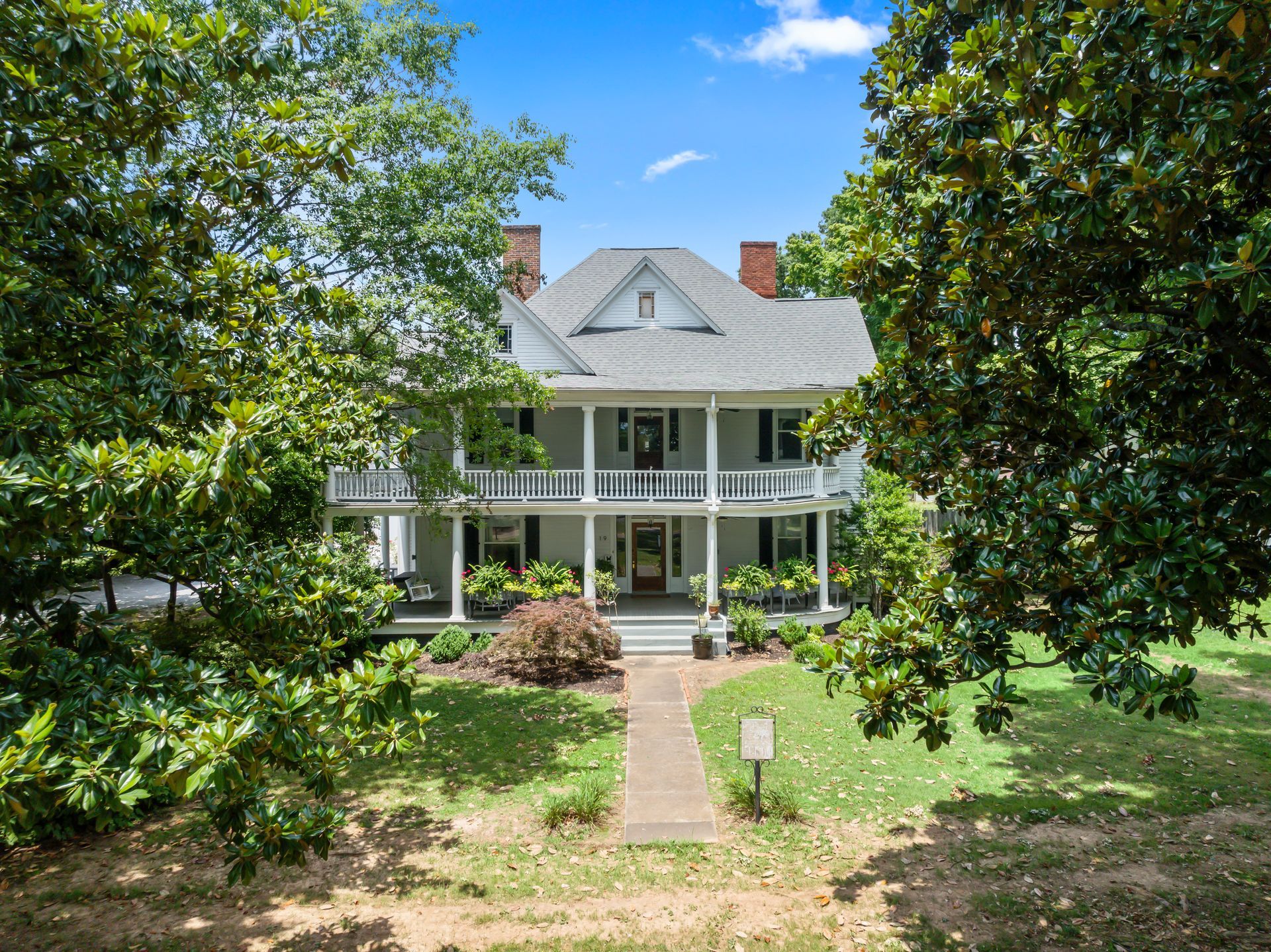 A large white house with a large porch is surrounded by trees.