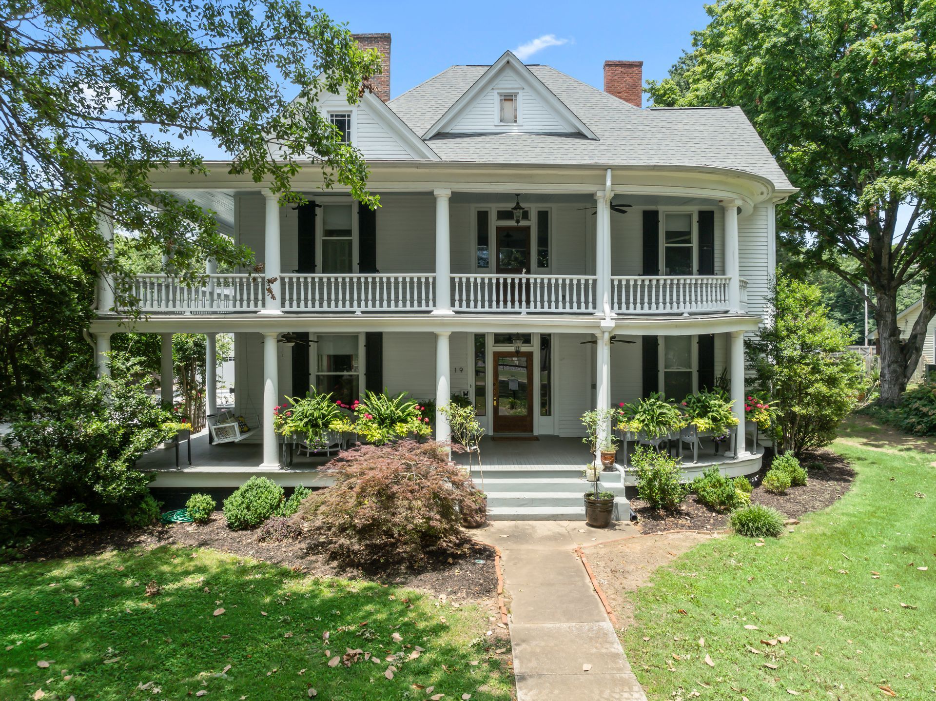 A large white house with a large porch on a sunny day.