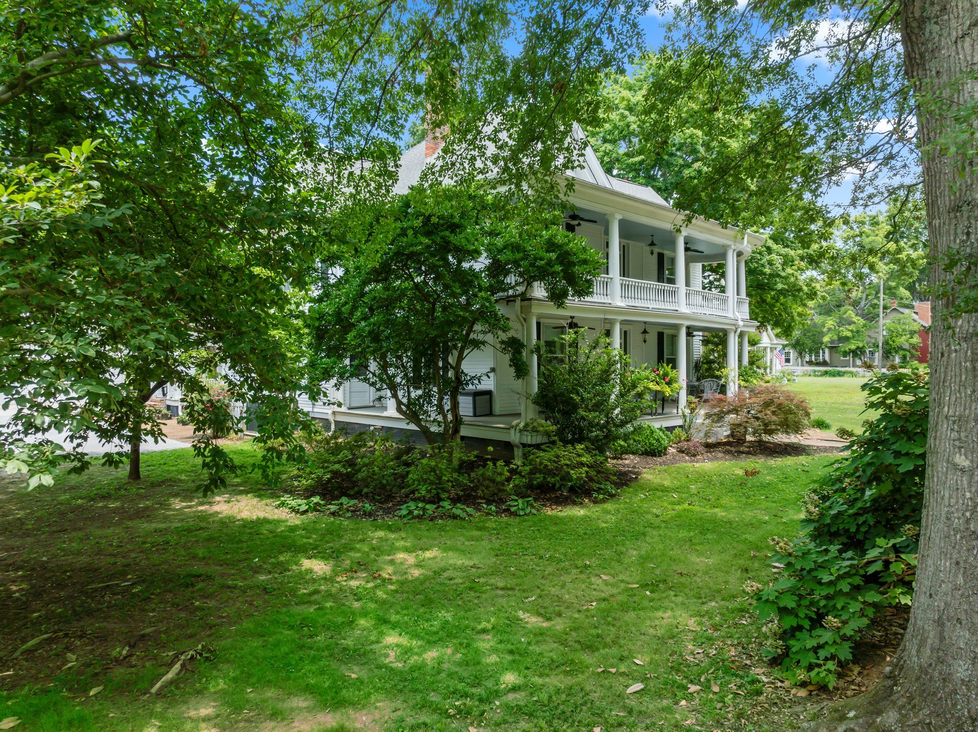 A large white house with a large lawn and trees in front of it.