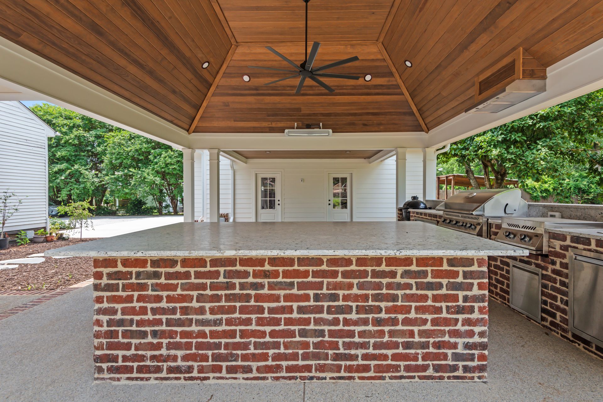 A large brick counter top under a wooden ceiling with a ceiling fan.
