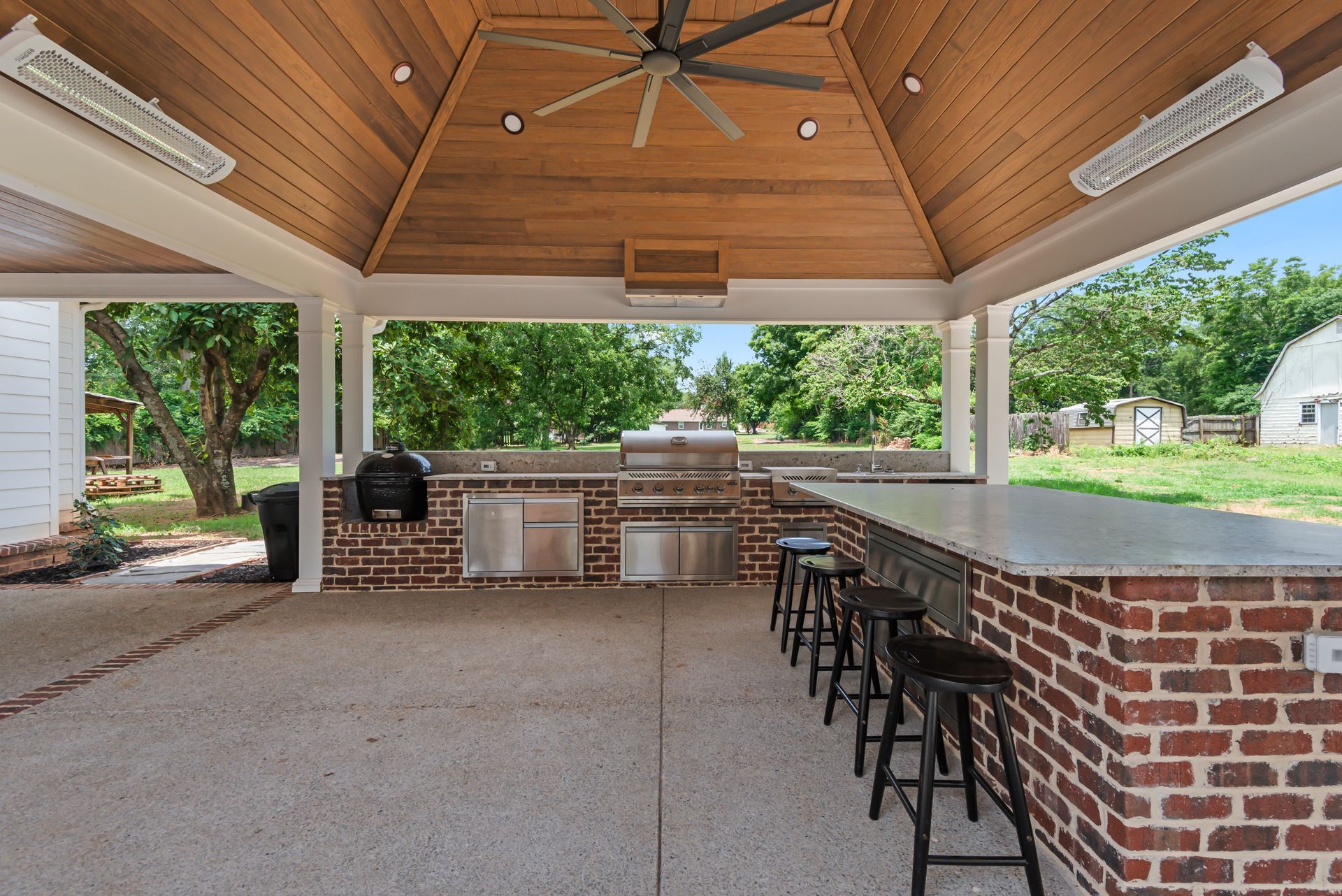 A large outdoor kitchen with a brick counter top and a ceiling fan.