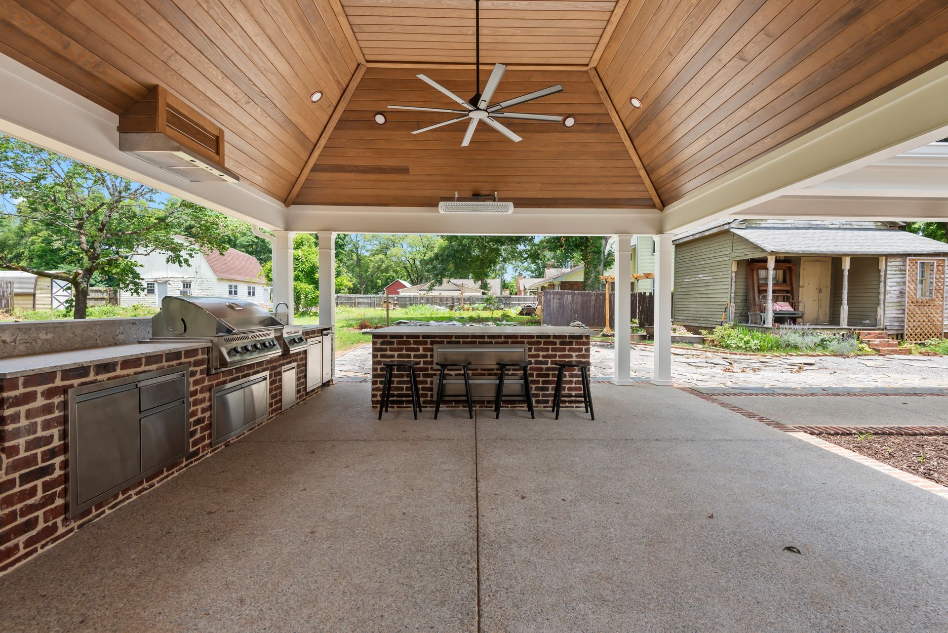 A large outdoor kitchen with a wooden ceiling and a ceiling fan.