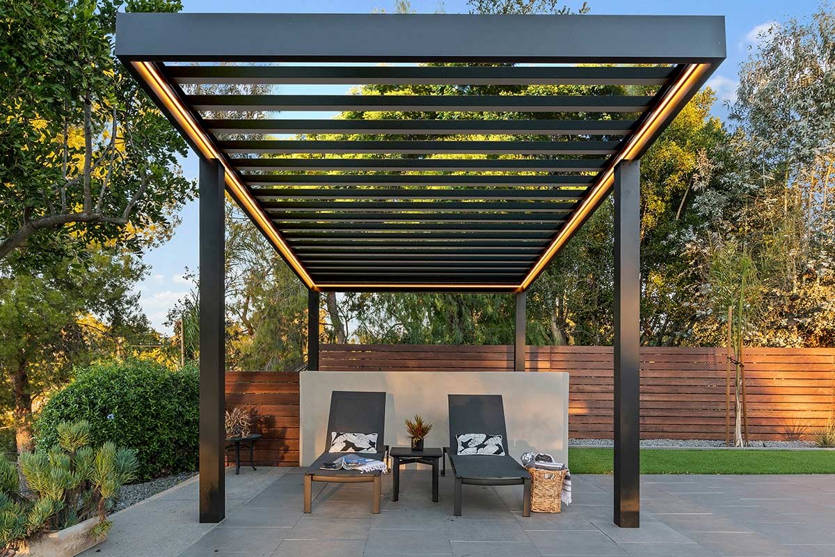 a pergola with chairs and a table underneath it in a backyard .