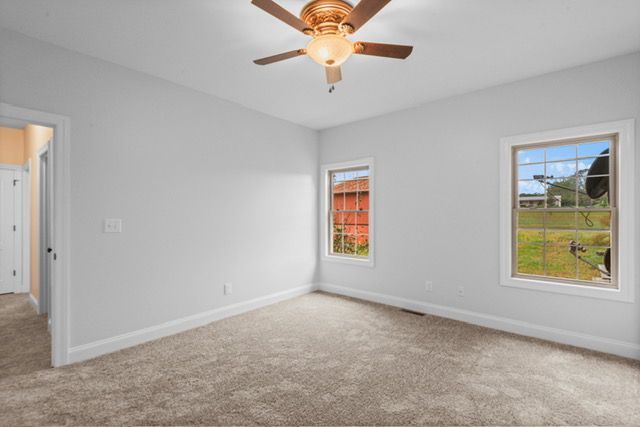 An empty bedroom with a ceiling fan and two windows. By Mims custom home construction