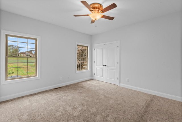 An empty bedroom with a ceiling fan and two windows. By Mims custom home construction
