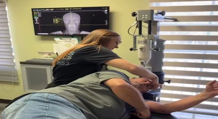 Woman adjusting a man's neck with an instrument in a medical setting, monitor displaying scan. Woman adjusting a man's neck with an instrument in a medical setting, monitor displaying scan.