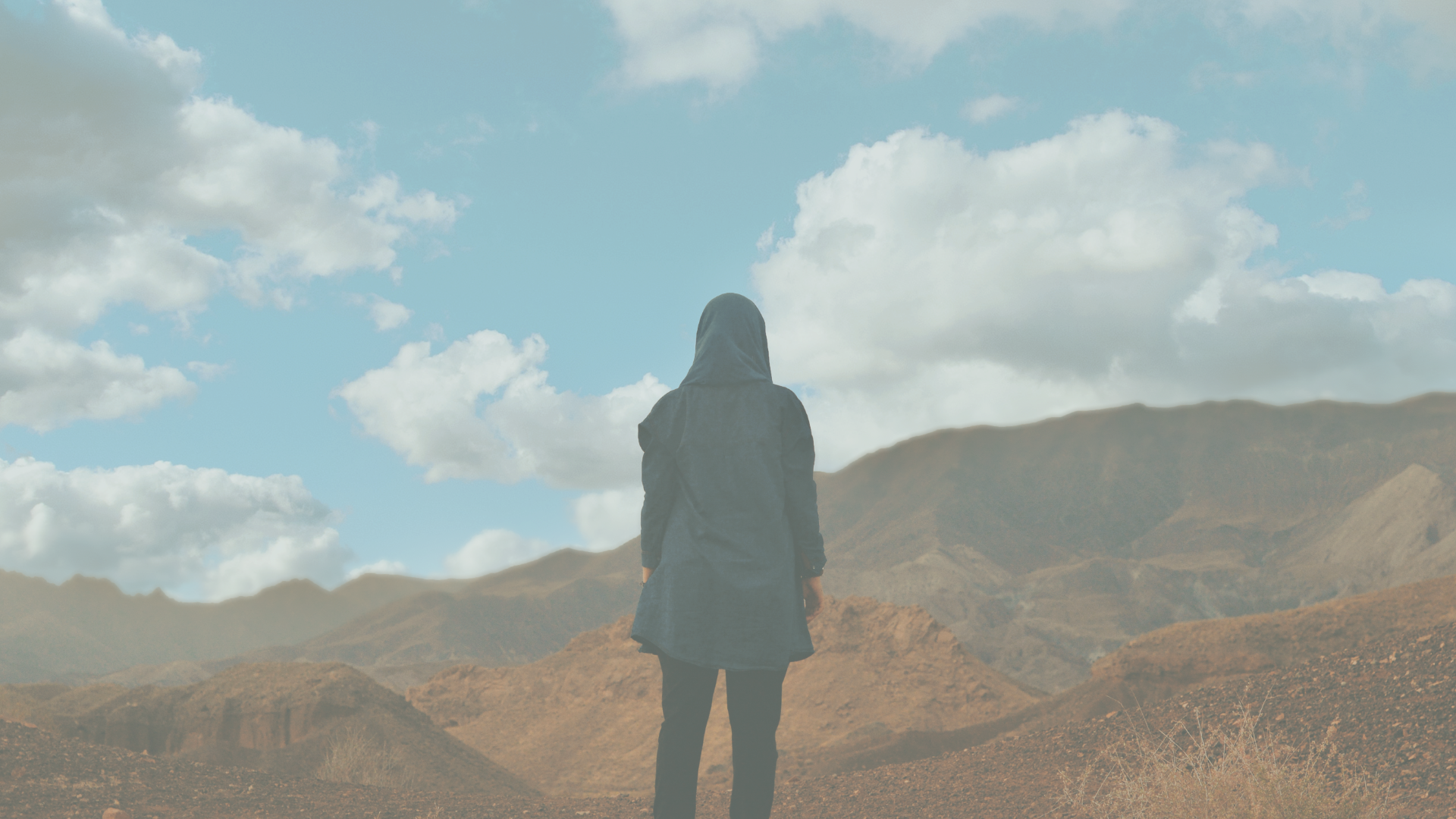 uma mulher está parada no meio de um deserto olhando as montanhas.
