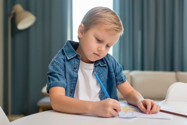 um menino está sentado a uma mesa desenhando com um lápis azul.