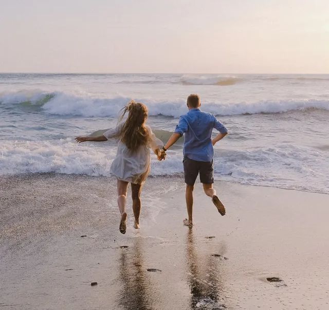 Um homem e uma mulher correm na praia de mãos dadas.