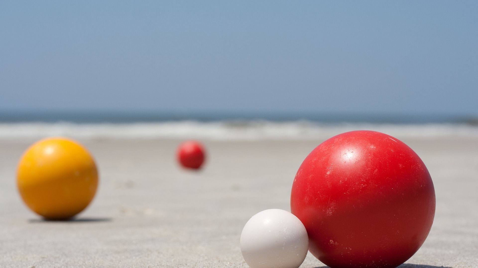 três bolas de bocha estão na areia de uma praia.