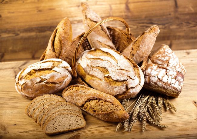Persona che tiene in mano una pagnotta di pane e ne mostra altre, in un panificio.