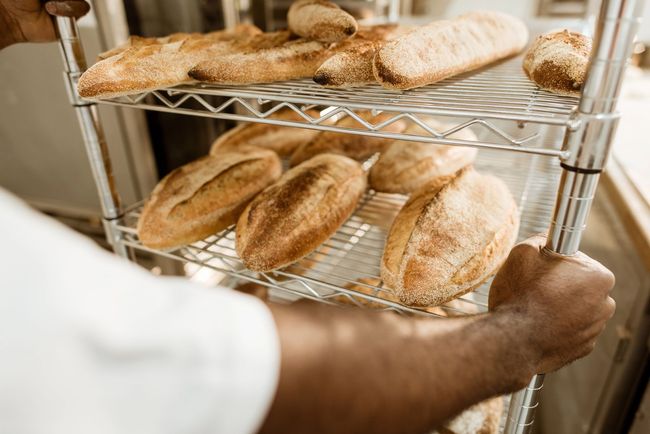 Persona che tiene in mano una pagnotta di pane e ne mostra altre, in un panificio.