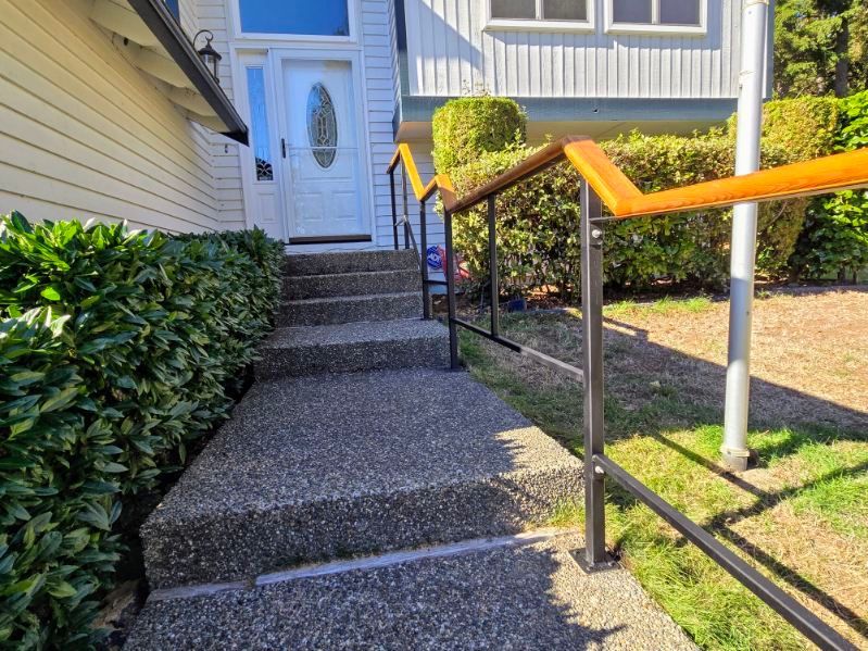 A concrete walkway leading up to a house with stairs and a railing.