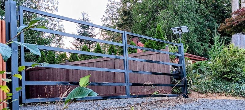 A metal gate is sitting on top of a gravel driveway next to a wooden fence.