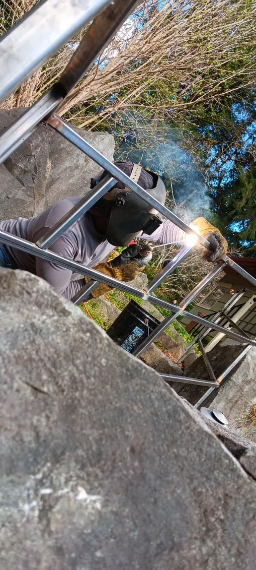 A man is welding a metal railing on a ladder.