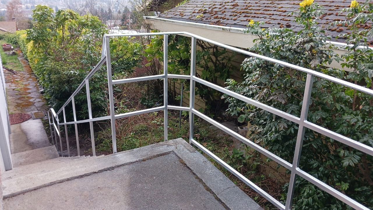 A metal railing surrounds a set of stairs leading up to a house.