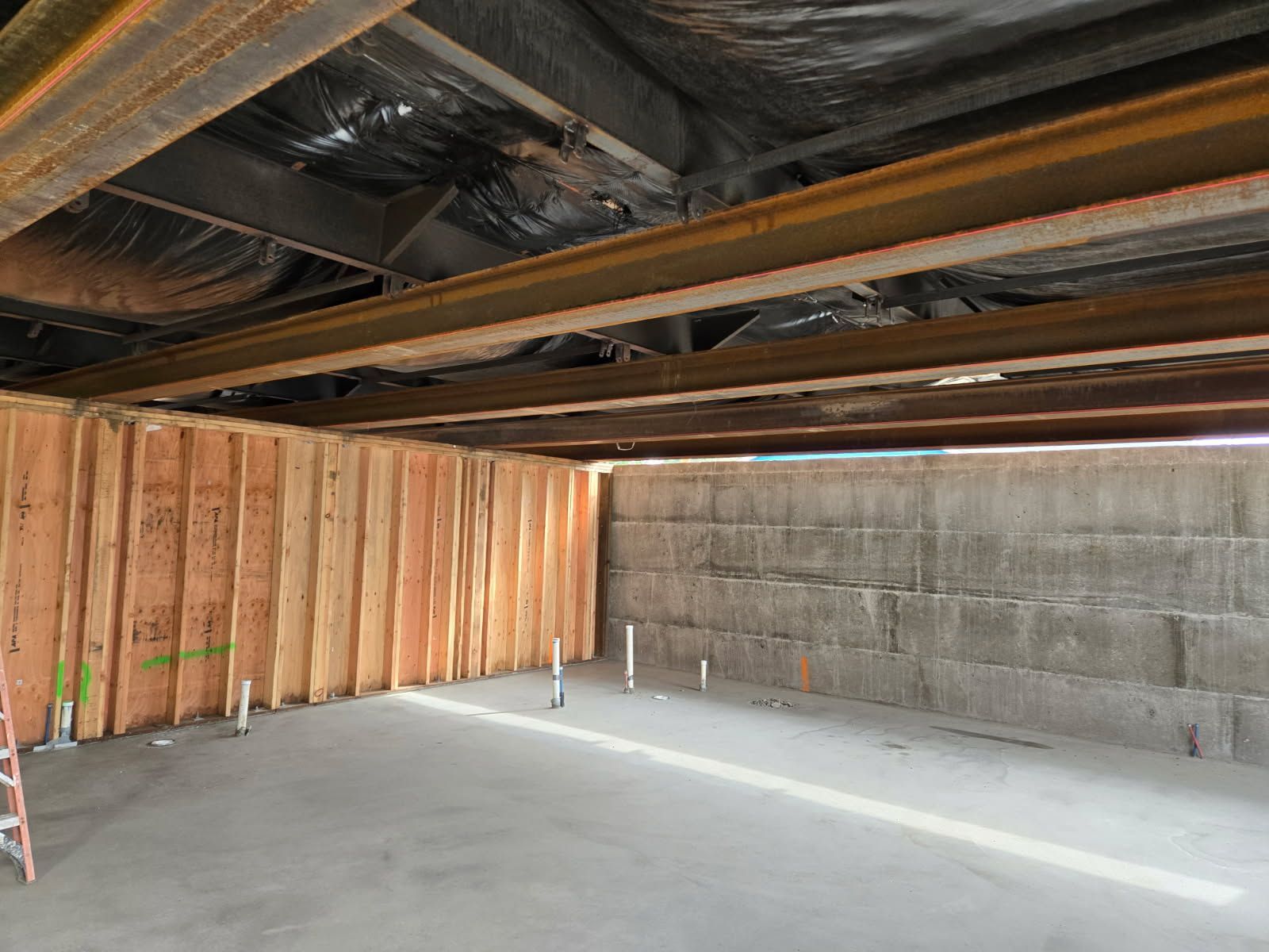 A basement under construction with wooden beams and a ladder.