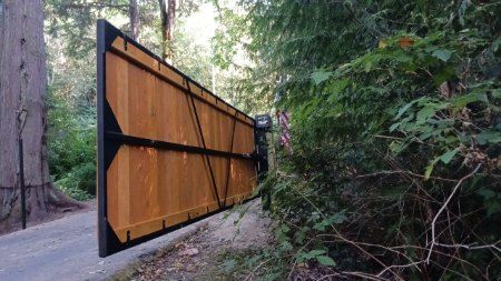 A wooden gate is sitting on the side of a road in the woods.
