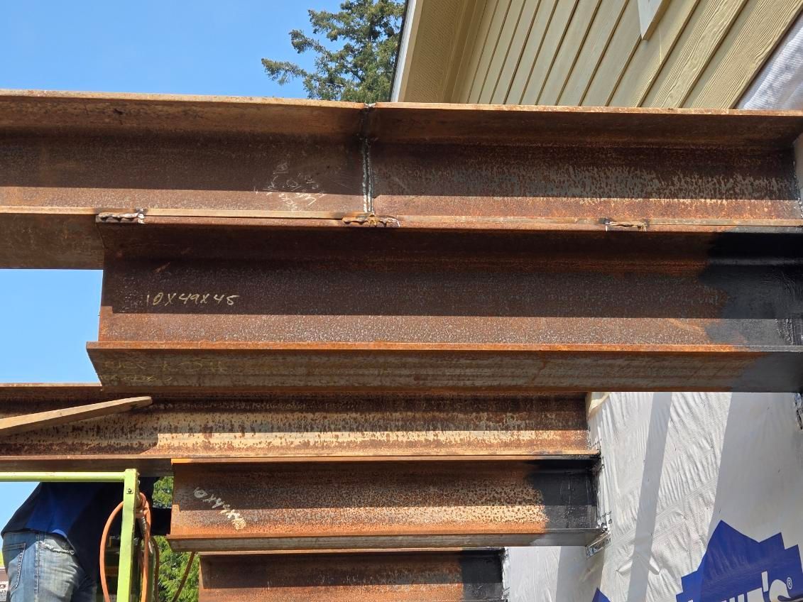A man wearing a mask is standing under a pile of rusty metal beams.