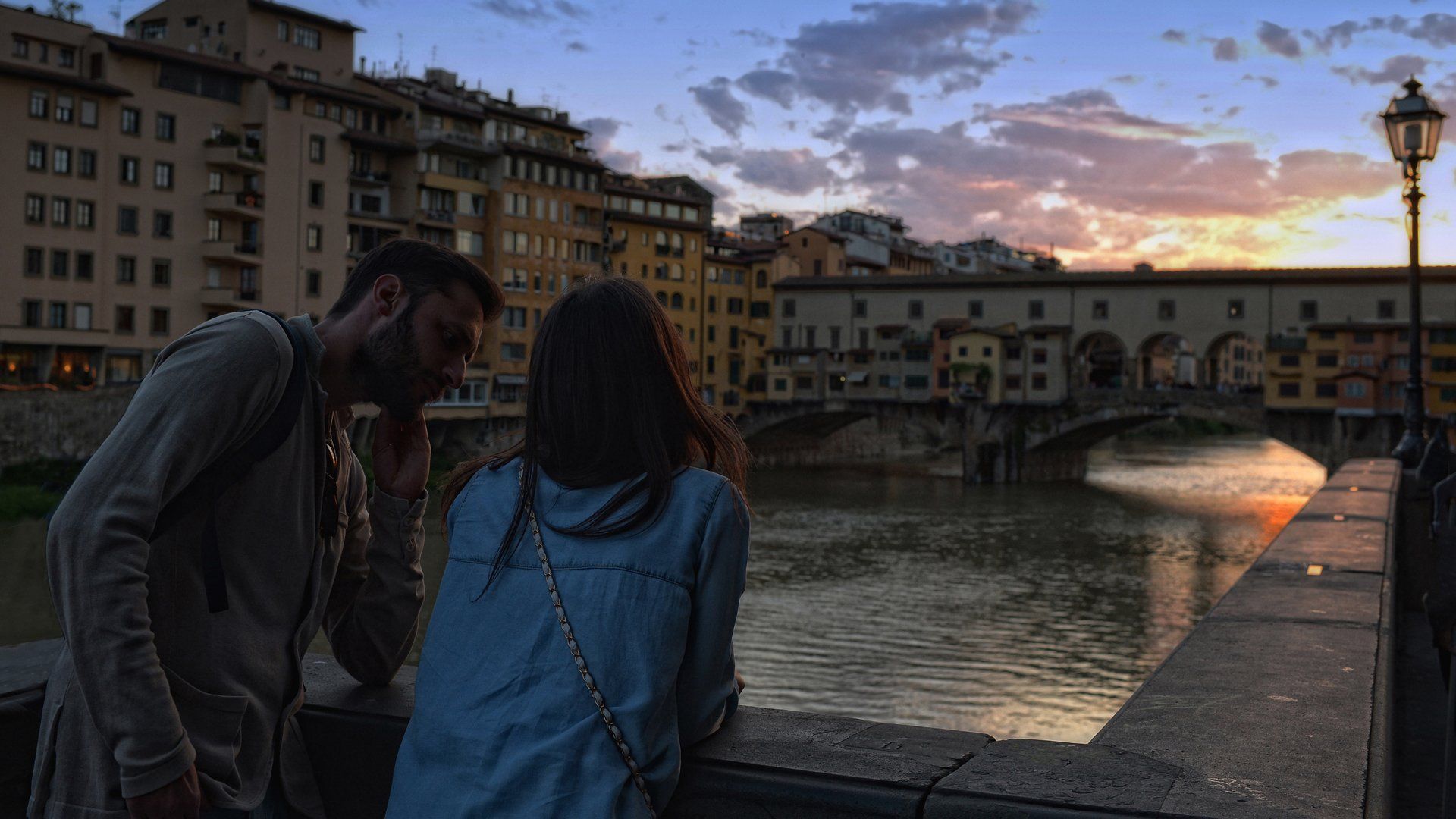 A man and a woman are standing on a bridge overlooking a river.