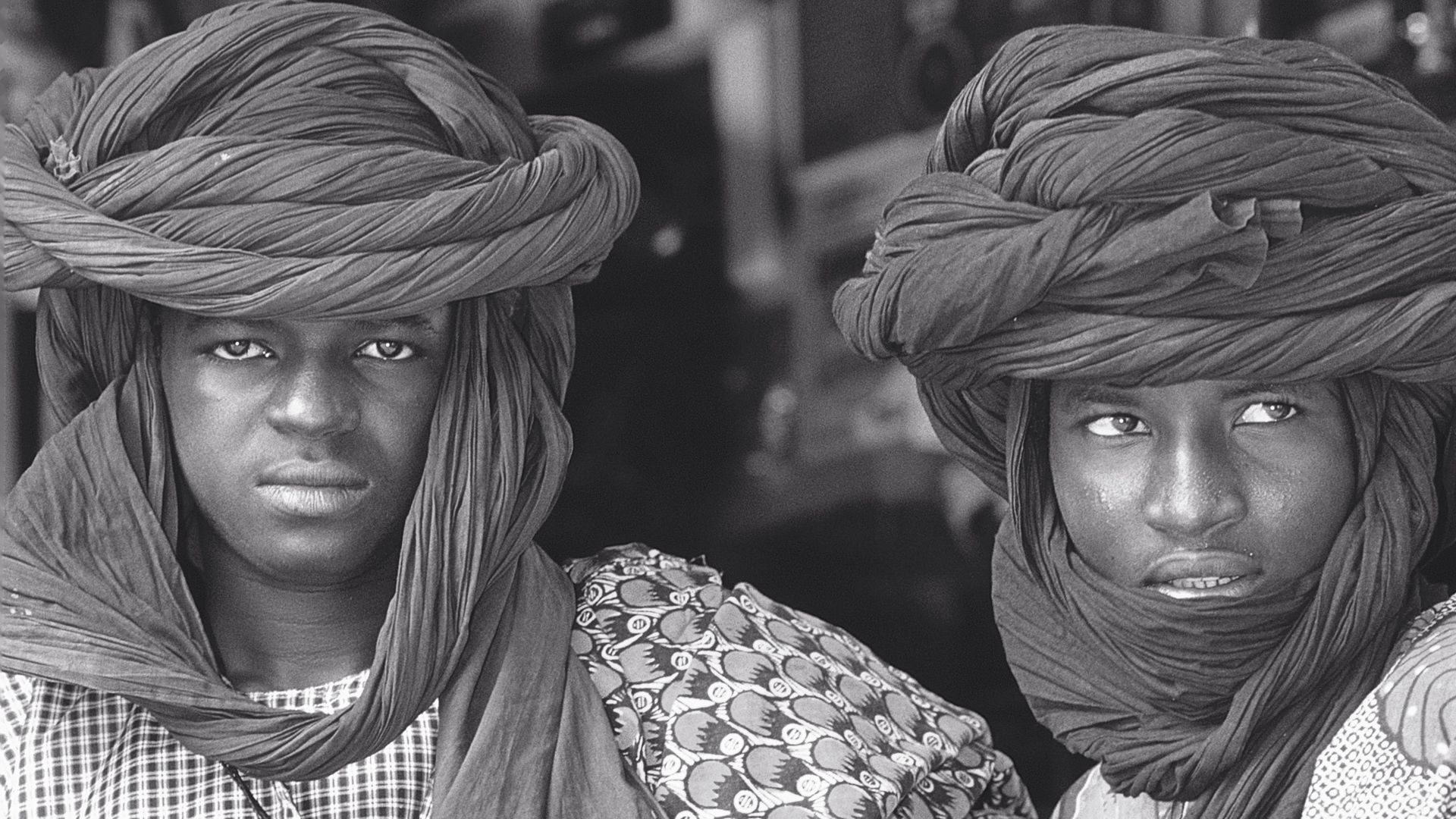 An elderly woman is looking out of a window with green shutters.