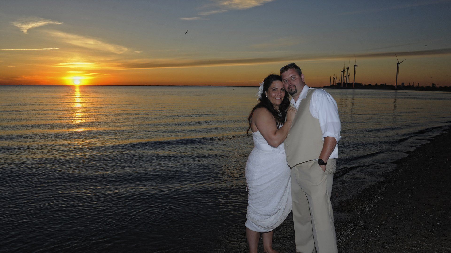 A bride and groom are posing for a picture on the beach at sunset.
