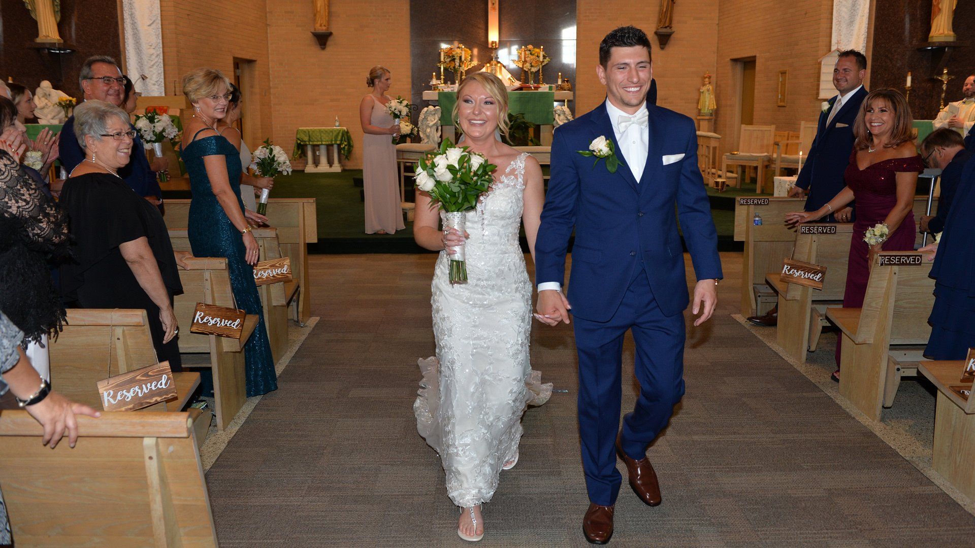 A bride and groom are walking down the aisle of a church holding hands.