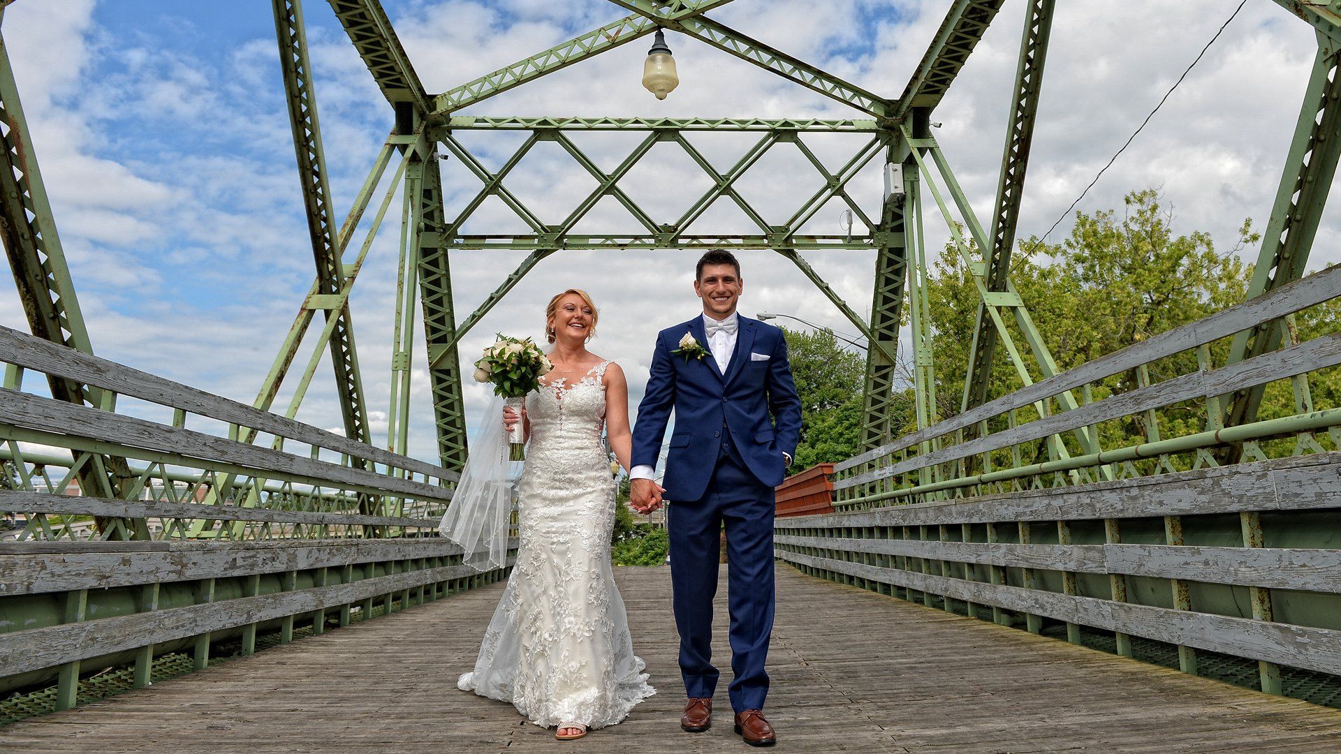 A bride and groom are walking across a bridge holding hands.